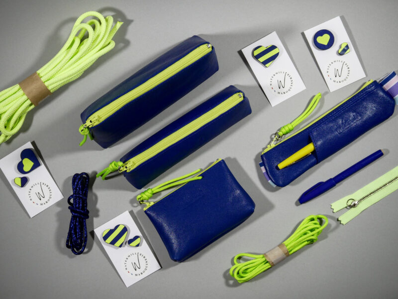 Accessoires Capsule Watermill — famille Berlingot en trois tailles : porte-monnaie XS, trousse S et grande trousse M, en cuir bleu roi avec zip contrasté jaune fluo, pin's cœur bicolores et cordons paracord assortis.
