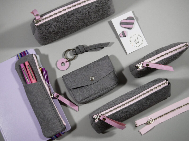Accessoires Capsule Watermill — famille Berlingot en trois tailles : porte-monnaie XS, trousse S et grande trousse M, trousse élastique, clutch , porte-clés et pin's, en croûte de cuir gris clair et zip contrasté rose pastel