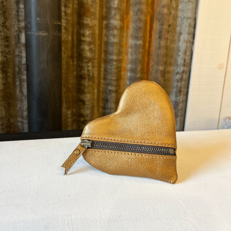 Porte-monnaie cœur en cuir doré avec fermeture zippée présenté sur fond de tôle d'atelier