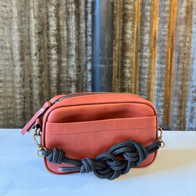 Sac à main camera case, en cuir avec poche avant, de couleur brun fauve, avec bandoulières cuir et corde et posé devant tôle d'atelier